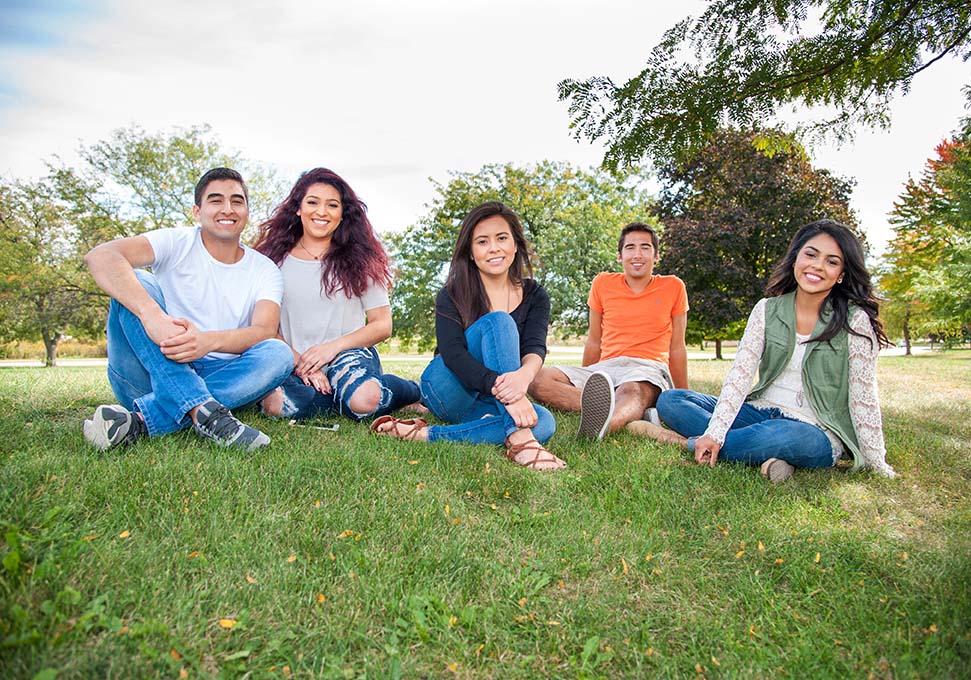 five Latino students sitting on grass smiling